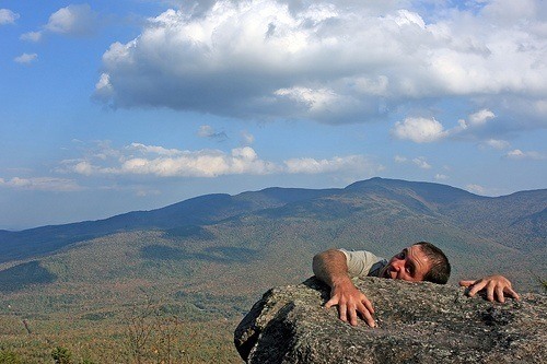 man clings to a boulder, embracing adventure against a stunning autumn landscape.