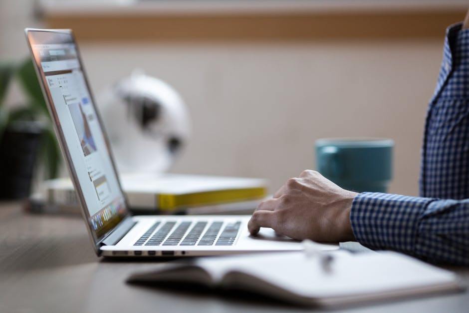 person typing on a laptop in a cozy, organized workspace with notebook and mug.