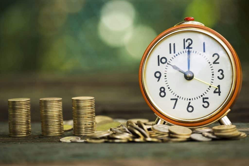 vintage alarm clock surrounded by coins highlights the connection between time and money.