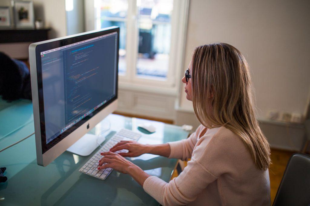 woman coding at a sleek desk in a bright, modern workspace.