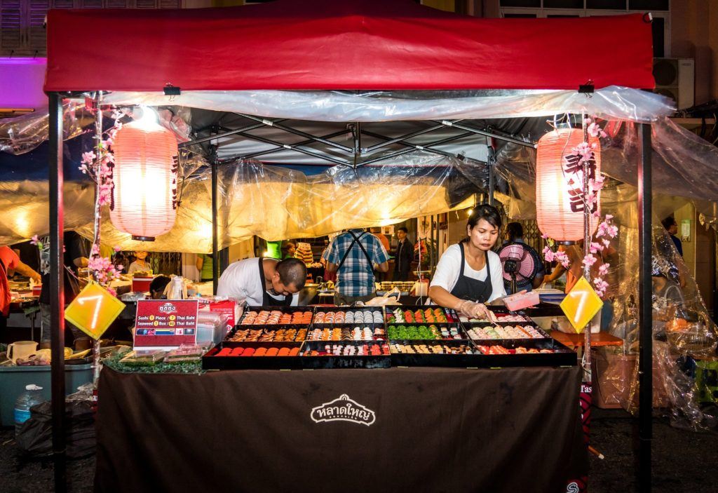 colorful sushi stall at a lively night market, with a focused vendor and festive atmosphere.