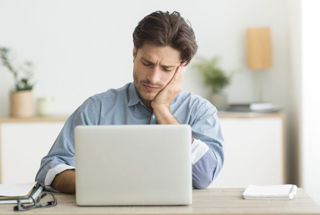 young man in a blue shirt deep in thought at a laptop in a serene workspace.