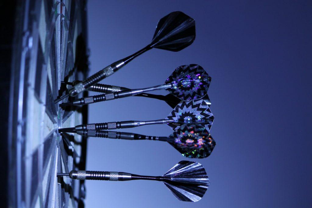 darts expertly aimed at a dartboard, highlighting precision in competitive gameplay against a blue backdrop.