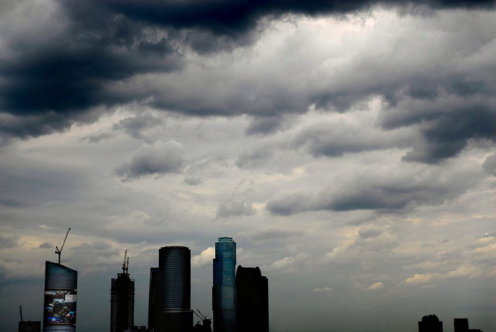 urban skyline with modern skyscrapers under dramatic, stormy clouds signifies growth amid natural challenges.