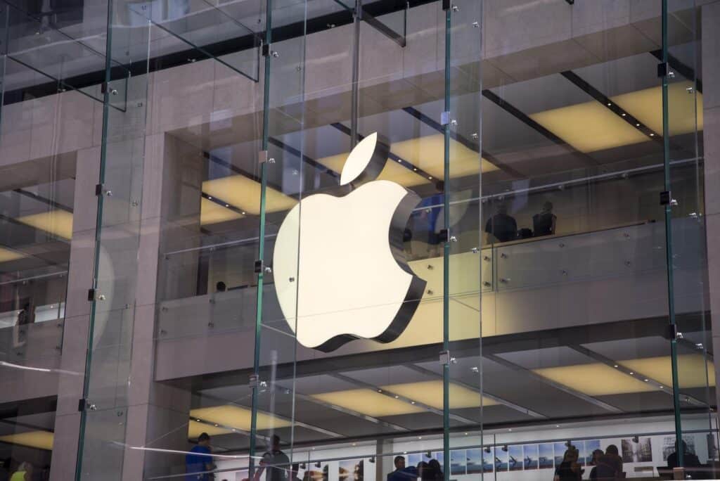 illuminated apple logo on a sleek storefront with shoppers inside a modern retail space.